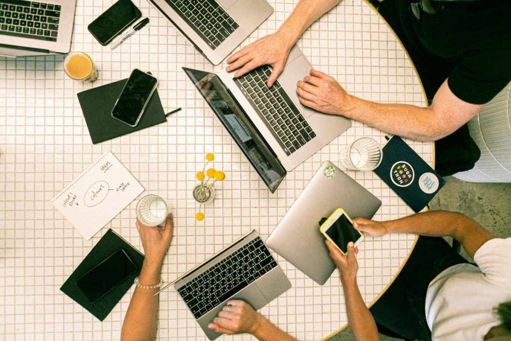 Top view of a team collaborating with laptops, phones, and notes in a modern office.